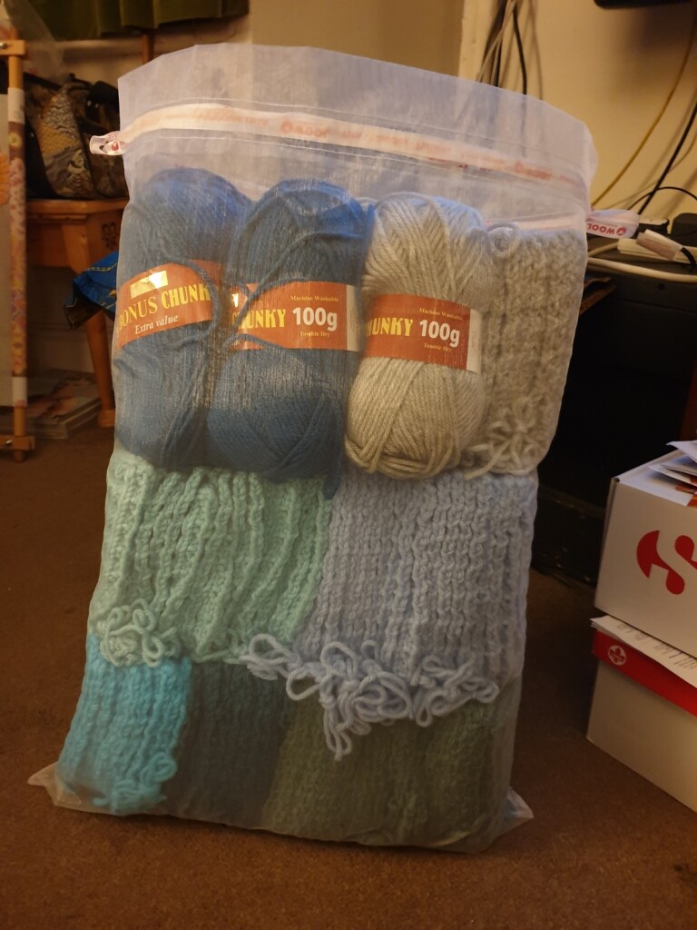 a large mesh bag full of knitted squares and also 6 balls of wool