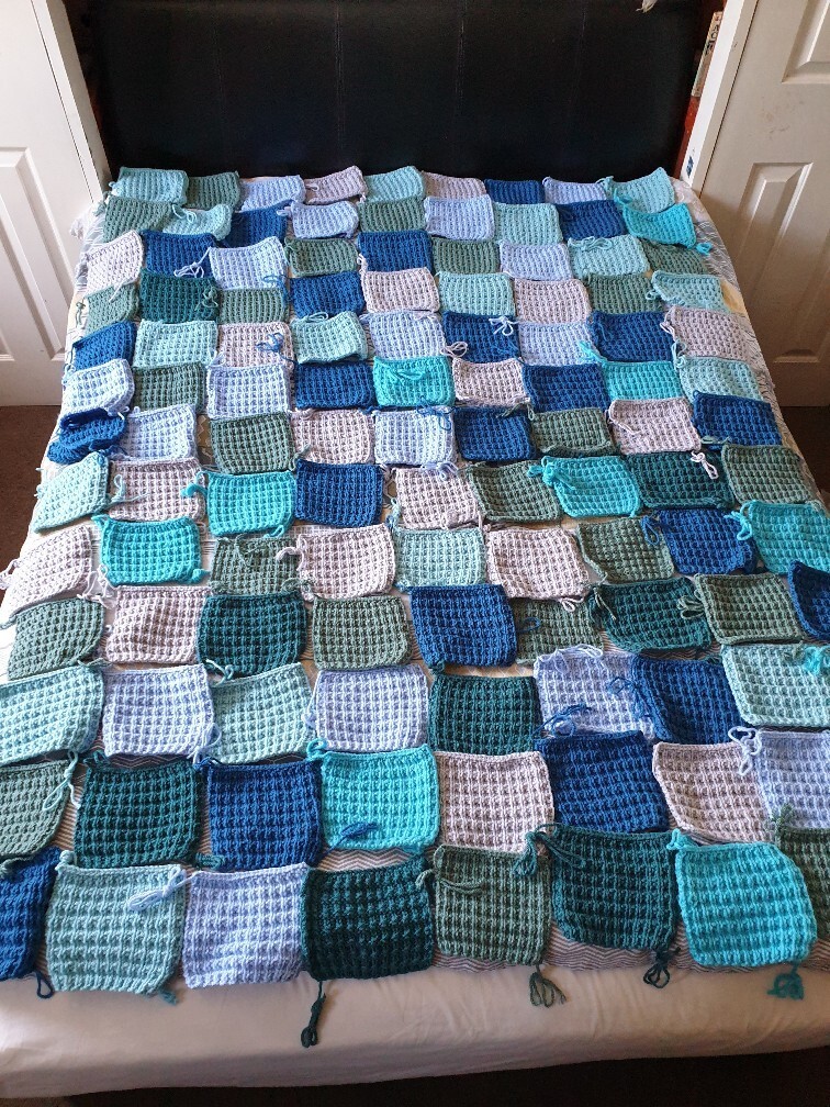 blue green and grey blanket squares are arranged randomly, covering a double bed