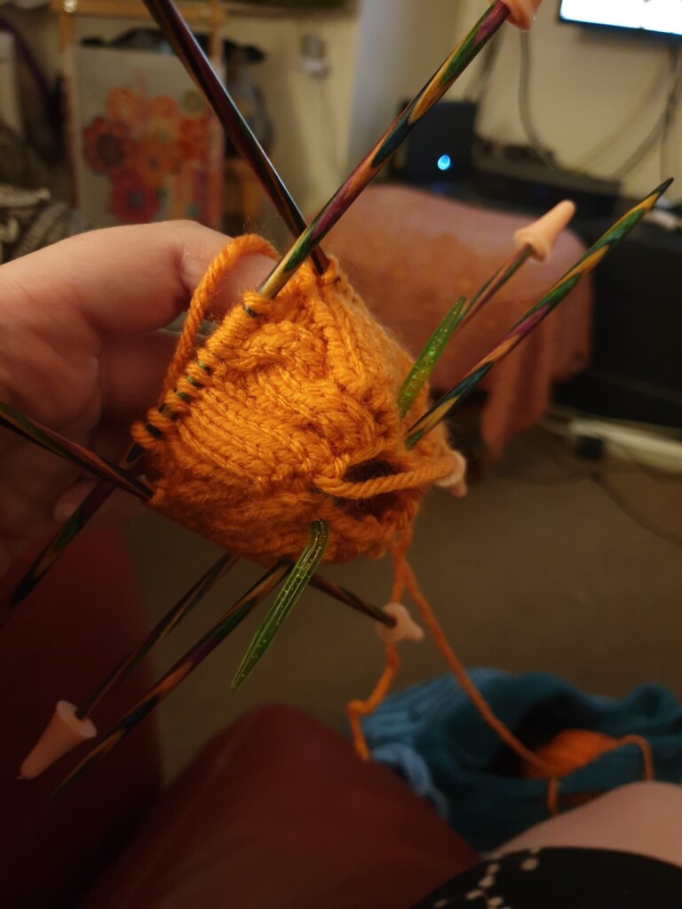 my current piece of knitting is orange wool on four double-pointed needles, with a cable design