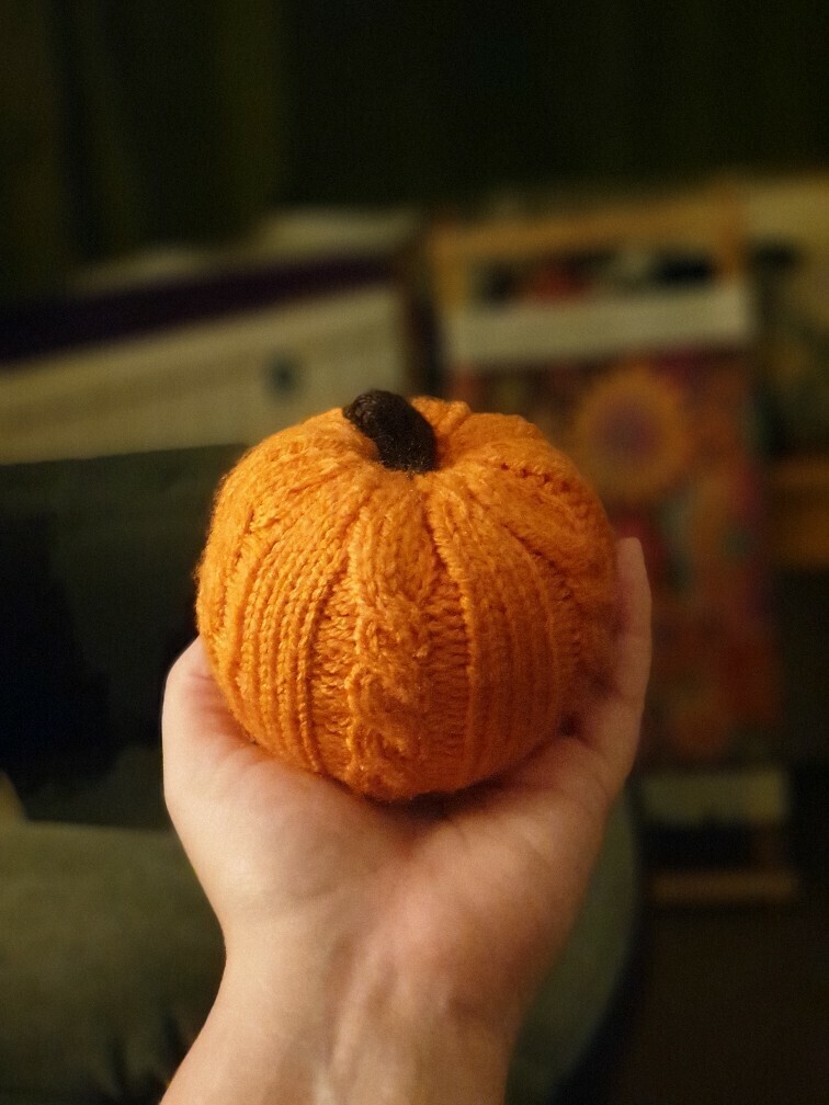 a small round knitted pumpkin fitting the palm of my hand, with cable designs down the edge