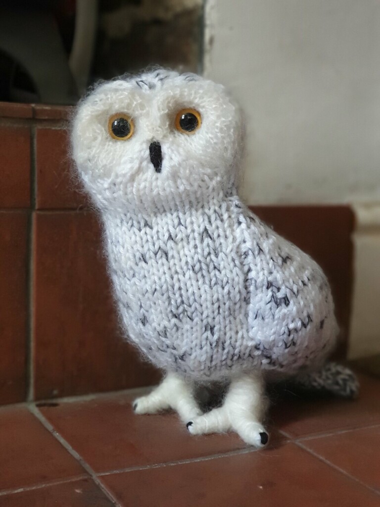 a knitted snowy owl sitting on red tiles