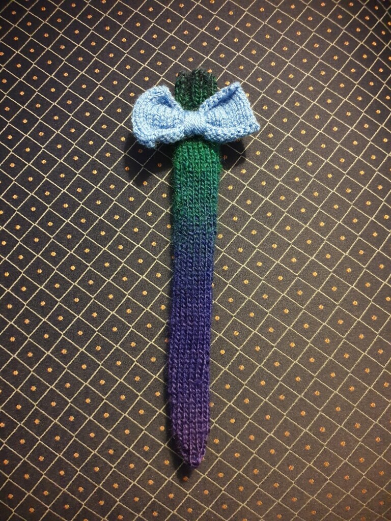 a purple and green knitted tail sock for a cat with a baby blue knitted bow at the top
