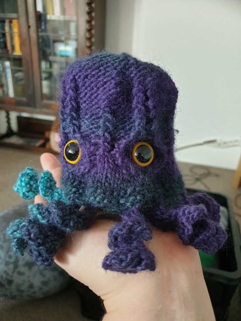 a purple and green tentacled dice bag with big eyes