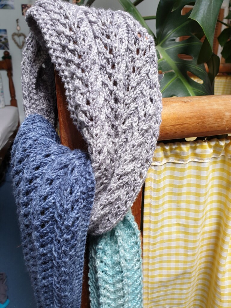 a light blue, navy and grey scarf wrapped around a banister to show it off, it has an intricate lace pattern