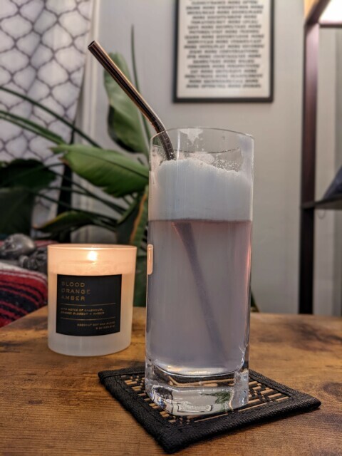 A lilac-colored cocktail with a thick head of foam, taken in my living room