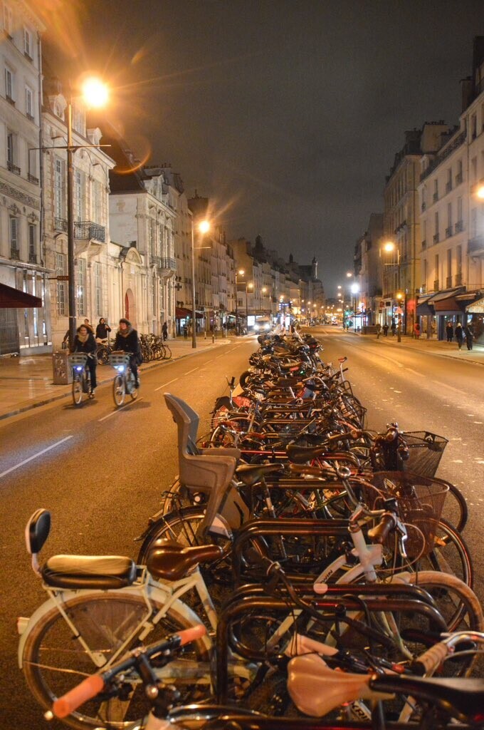 A row of parked bicycles sits between two car lanes and a bidirectional protected bike lane on a street in Paris.