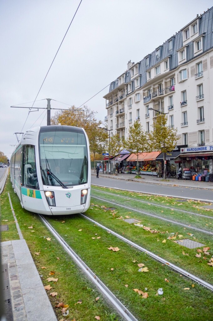 A modern white tram glides across a grass tramway in the 18th arrondissement of Paris. A five storey apartment building can be seen in the background.