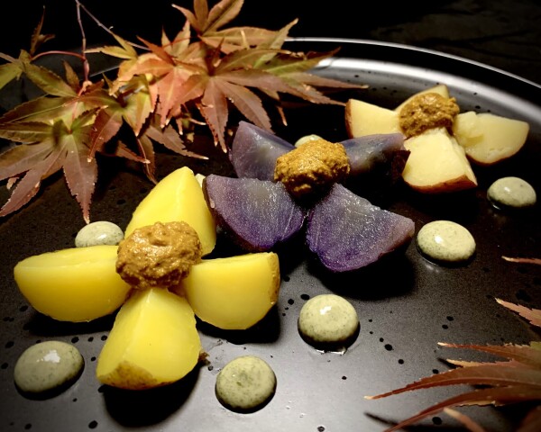 On a black plate, branches of reddening maple leaves, still partly green, emerge from the top left and bottom right of the image. Centred in a diagonal from bottom left to upper right are colourful potatoes, chopped in quarters and splayed out like flowers. A yellow potato, a purple potato and a white potato. On top middle top of the potatoes, like the head of a flower is a round dollop of acorn miso sauce. Surrounding the potatoes are flattened spheres of sissoo-ezu. 

This version of sissoo-ezu was basically, dried sissoo leaves ground to powder and mixed with silken tofu and tiny bit of mustard and vinegar. 