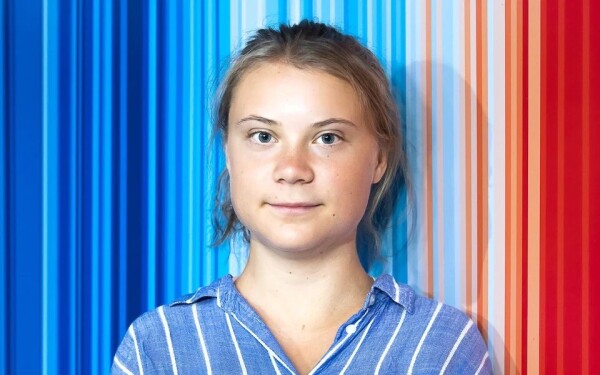 Head shot of Greta Thunberg, standing in front of the familiar "climate stripes" graphic.