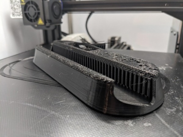 An oblong 3D-printed object made of black plastic. About half a centimeter from the top, the layers of material start looking pockmarked and rough, instead of smooth.