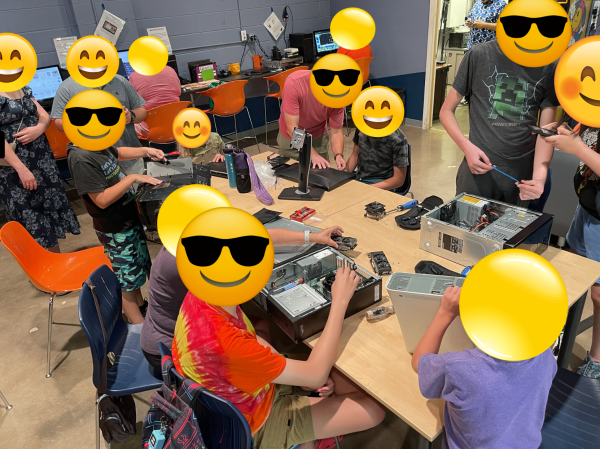 A group of people sitting around a table with electronics in various states of disrepair.