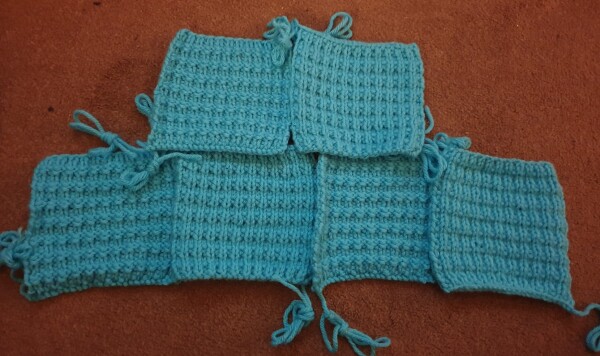 six light blue knitted squares are laid out on the floor