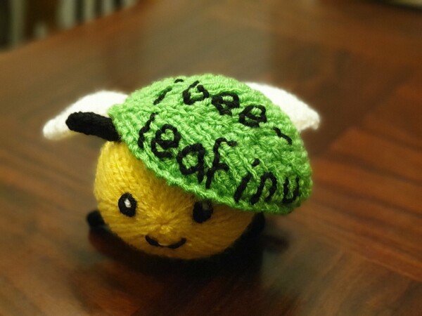 a cute round knitted bee underneath a leaf with embroidered writing on it