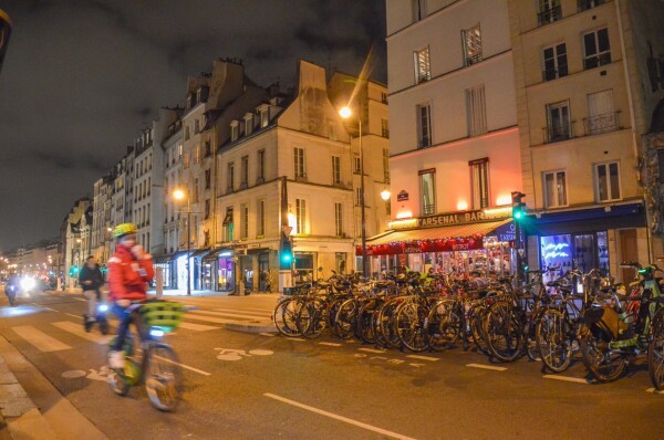 A cyclist rides along a bidirectional protected bike lane lined with parked bikes after dark on a street in Paris.