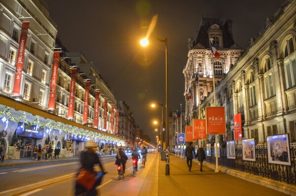 Several cyclists ride along a bidirectional protected bike lane after dark on a street in Paris.