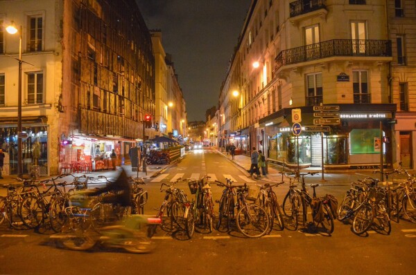 A cyclist rides along a bidirectional protected bike lane lined with parked bikes after dark on a street in Paris.