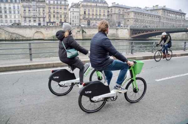 Three cyclists—two on shared e-bikes—use a car-free street on the banks of the River Seine in Paris.