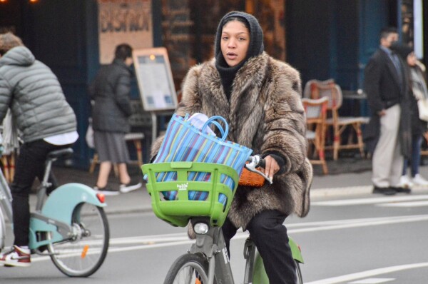 A woman in winter attire rides a green and silver shared bicycle along a protected bike lane on a street in Paris.