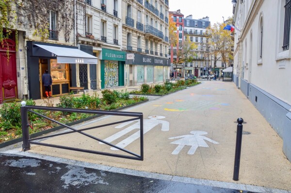 A car-free “school street” in Paris includes bike parking, vegetated areas, and white asphalt painted with colorful games.
