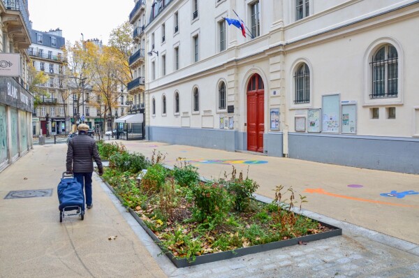 A car-free “school street” in Paris includes bike parking, vegetated areas, and white asphalt painted with colorful games.
