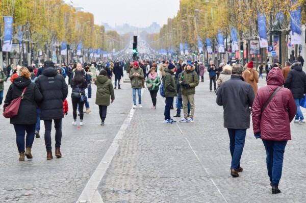 A large crowd of people walk on the car-free Avenue des Champs-Élysées in Paris. The Arc du Triomphe can be seen in the distance.