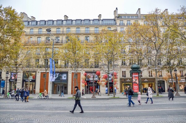 People walk on the car-free Avenue des Champs-Élysées in Paris. A six-storey building with ground level retail is in the background.