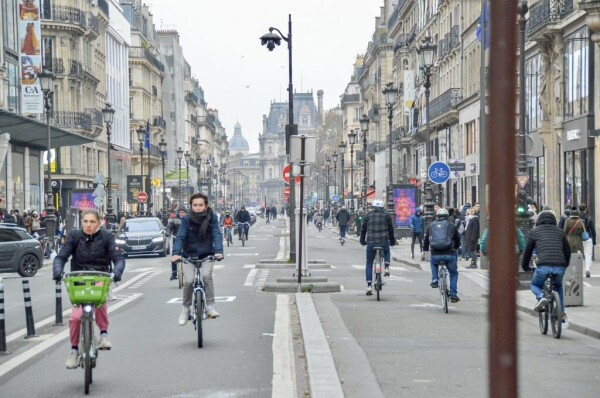 Several cyclists—both male and female—in casual winter attire ride on a protected bike lane along the Rue de Rivoli in Paris.