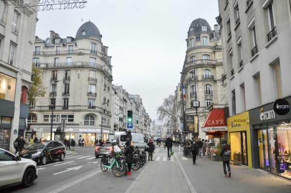 A male cyclist in casual winter attire rides on a unidirectional protected bike lane along the Rue de Saint Antoine in Paris.